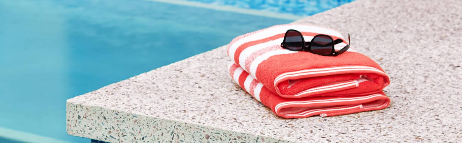 a neatly folded beach towel and sunglasses resting on the edge of a pool