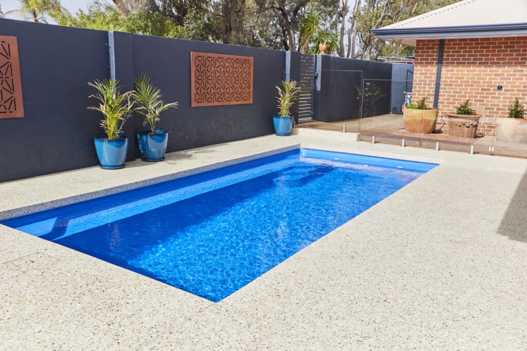 a rectangular shaped pool with a decorative concrete edge and potted palms along the wall