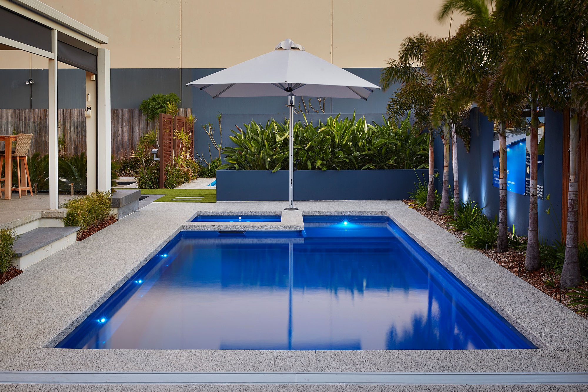 a pool with decorative concrete edging in a garden of palms and an umbrella