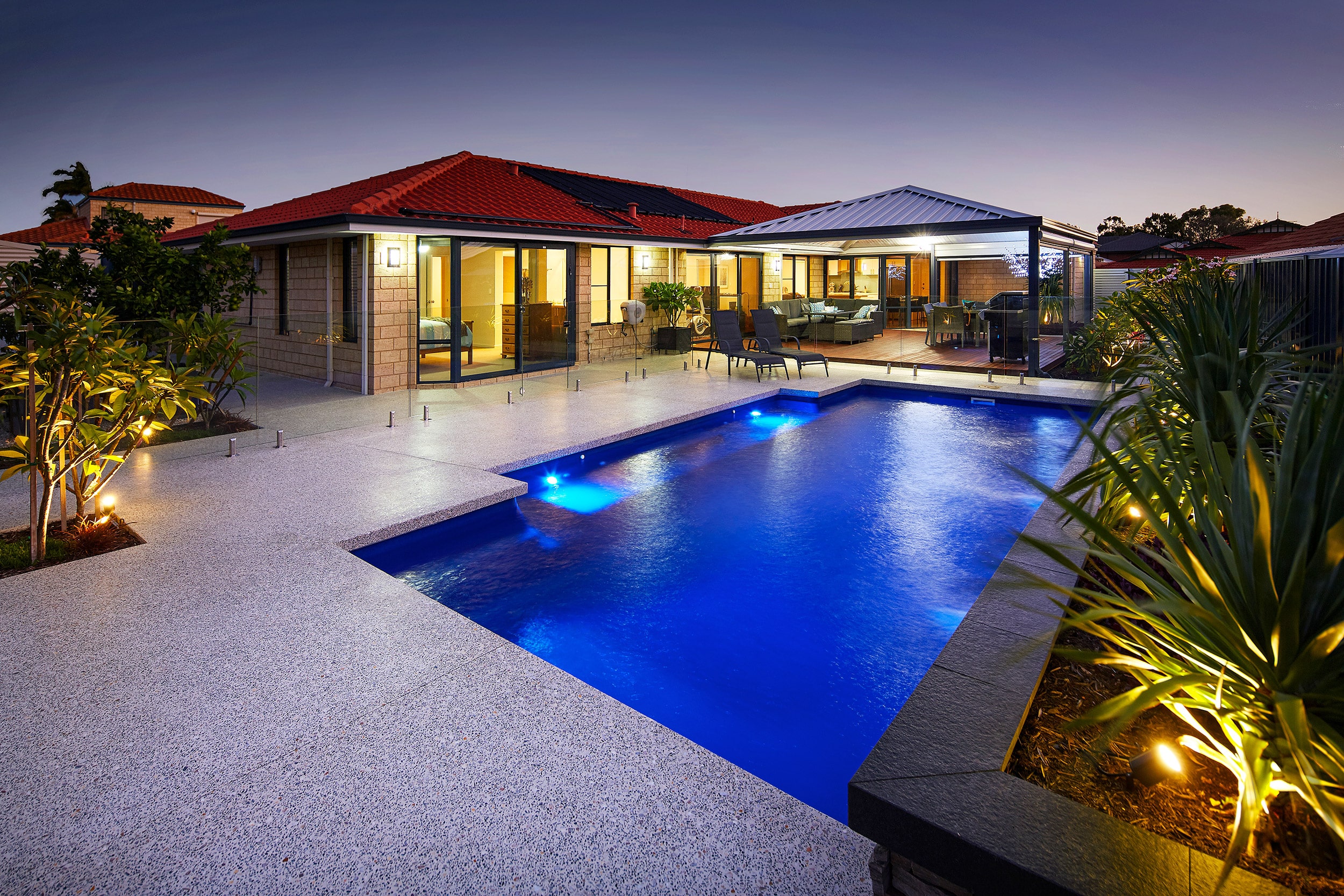 a nighttime shot of a large pool in the backyard of a house lit up by garden lights