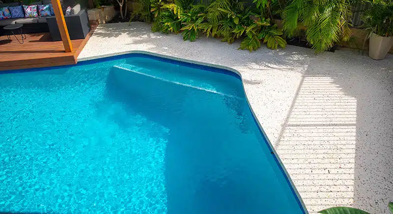 a curved pool edge with a garden and decking backdrop