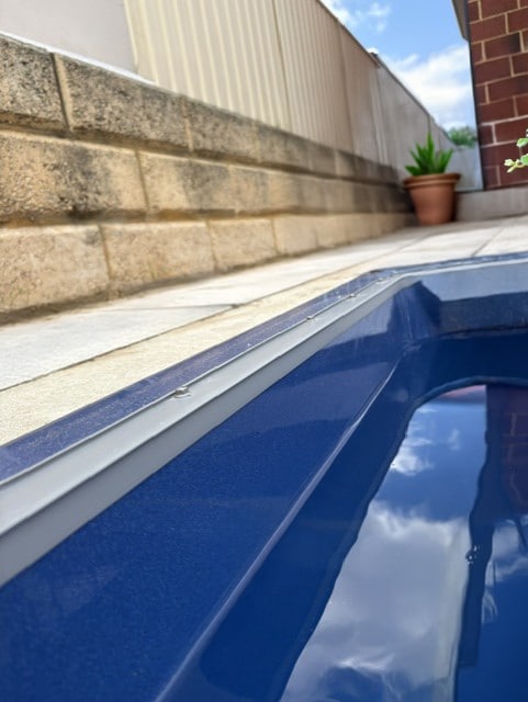 Close-up of a dark blue fibreglass pool shell edge alongside stripped besser block retaining wall, ready for coping installation